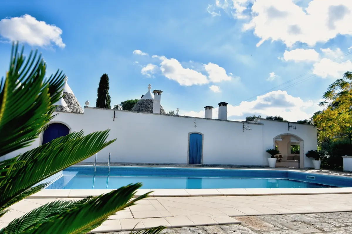 The pool with the trulli and the blue doors, through cycad leaves